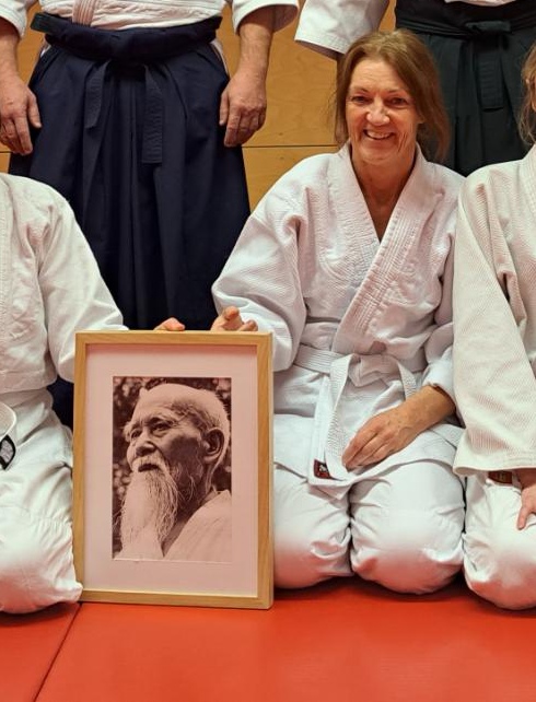 Marina de Greef im Aikido-Kampfdress. Sie hält ein Foto des Begründers der Sportart Ueshiba Morihei